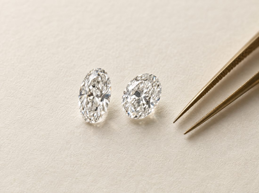 Two oval diamonds and jeweller’s tweezers on ivory paper
